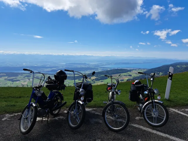 Vier Töffli am Strassenrand, unten der Neuenburgersee und die Alpen.